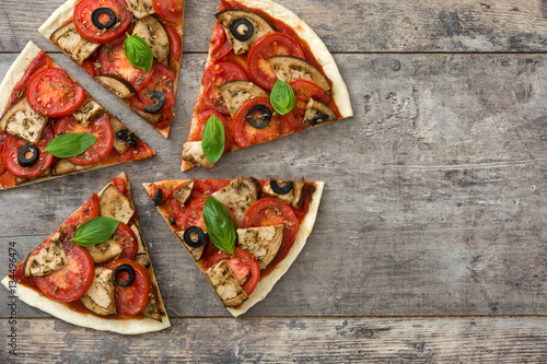 vegetarian pizza slice with eggplant, tomato, black olives, oregano and basil on wooden background.Top view