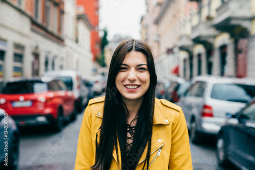 Portrait of young beautiful caucasian brown hair woman outdoor in the city looking at camera smiling - happiness, having fun, serene concept