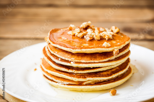 Pancakes with honey and walnuts on rustic wooden background