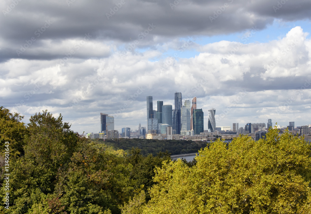 View of Moscow financial district and business center from the observation deck at Sparrow hills. Trees, Moskva river and dramatic clouds are in the view.