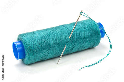 Green thread on a plastic spool with needle on white background