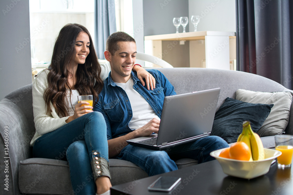 Beautiful young couple bonding to each other using laptop while sitting on the couch together. Beautiful young couple bonding to each other using laptop while sitting on the couch together.