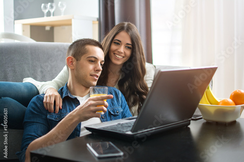 Cheerful couple searching something on laptop at home.