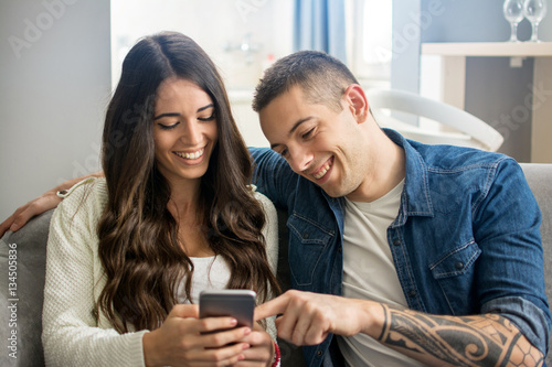 Cheerful young couple using smartphone. Boyfriend pointing something on phone to his girlfriend.