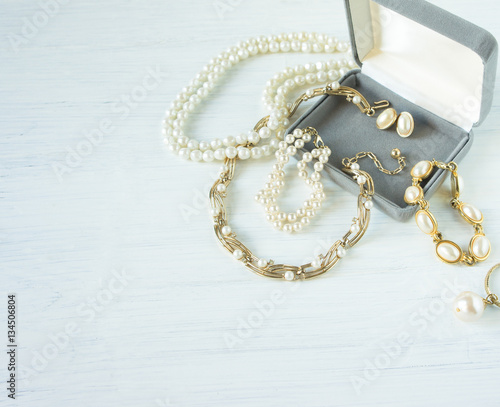 Woman's Jewelry. Vintage jewelry background. Beautiful gold and pearl necklaces, bracelets and earrings in a gift box on white wood. Flat lay, top view