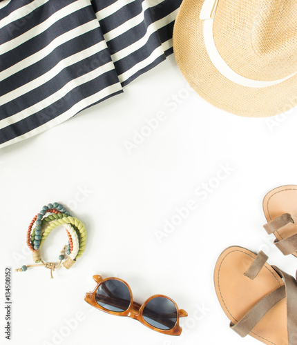 Summer fashion, summer outfit on white background. Blue striped dress, brown sandals, retro sunglasses, straw hat, wod bracelet. Flat lay, top view