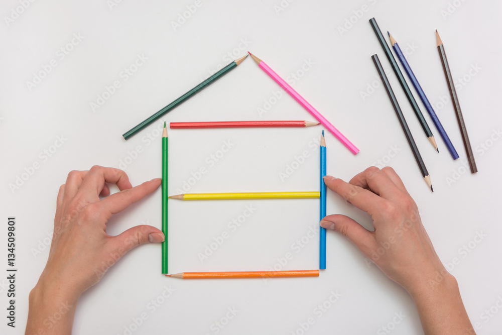 closeup Hands build a house on a piece of paper from the crayons, erecting walls closeup Hands build a house on a piece of paper from the crayons, erecting walls