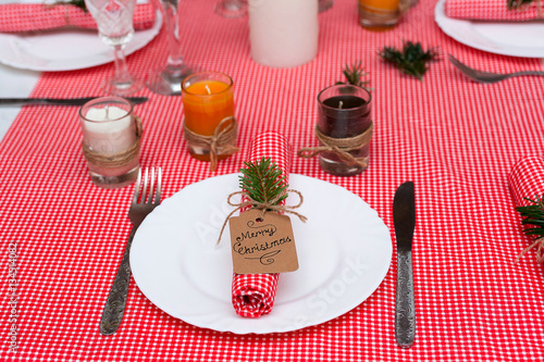 Festive composition with candles and plates. Table decoration. A beautiful table setting, red table cloth, tablecloth in the box. Christmas dinner. A Napkin decorated with inscription Merry Christmas.