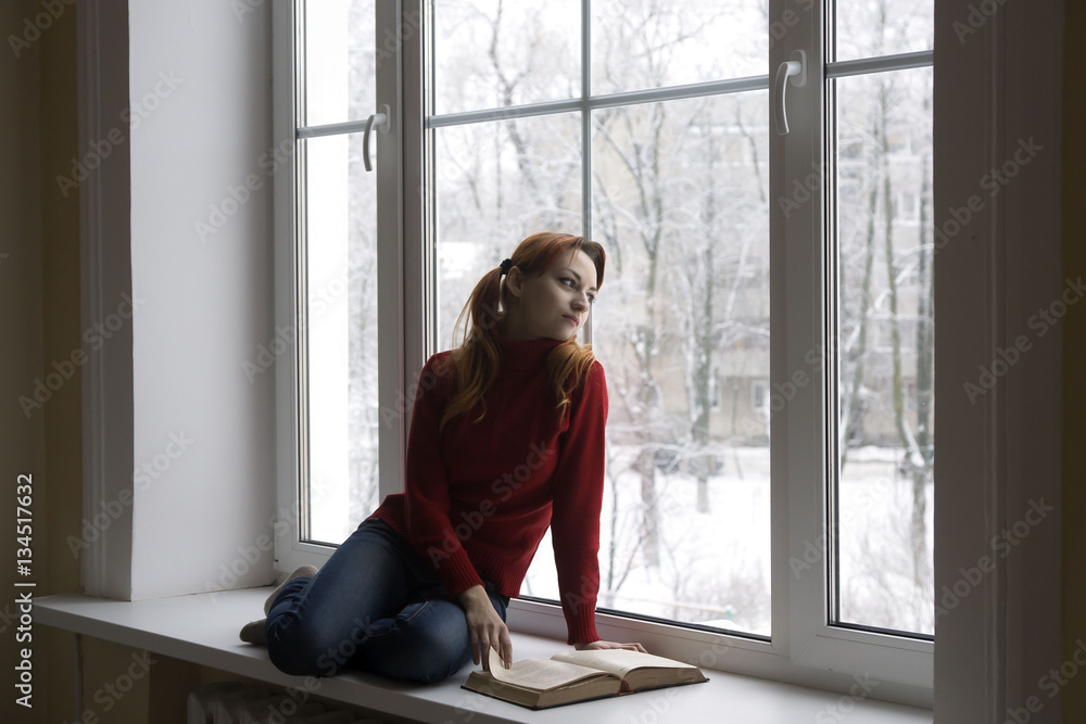 Thoughtful and dreaming girl looking out of the window while sitting on the window-sill Thoughtful and dreaming girl looking out of the window while sitting on the window-sill