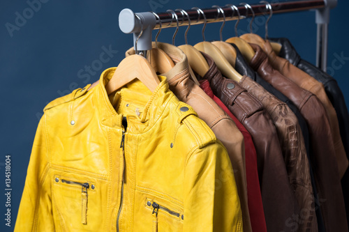 Different color leather jacket hanging on rack on blue background