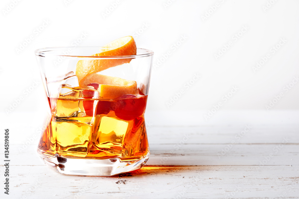 Glass of old fashioned whiskey with ice, orange and cherries over a white wood table Glass of old fashioned whiskey with ice, orange and cherries over a white wood table