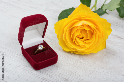 Golden diamond ring in a red gift box and yellow rose on white wooden background © d_zheleva