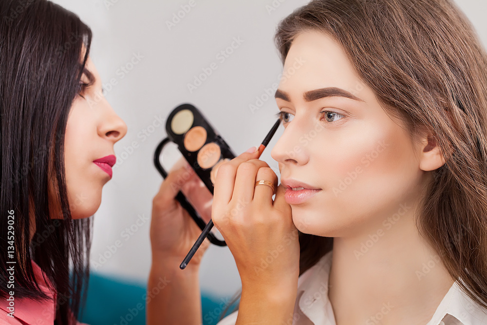 Make up artist doing professional makeup of young woman near the mirror in beauty studio Make up artist doing professional makeup of young woman near the mirror in beauty studio