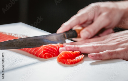 Hand with knife cuts fish. Raw fish on cooking board. Salmon meat for special dish. Chef prepares a delicacy