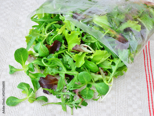 Fresh mixed greens leaf vegetables of arugula, mesclun, mache in open plastic bag