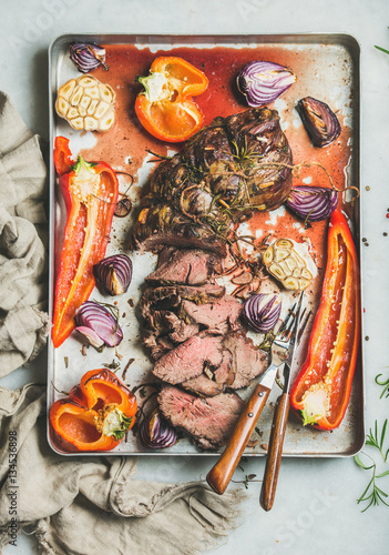 Cooked Roastbeef meat with roasted vegetables and herbs in metal baking tray over grey marble background, top view. Slow food concept