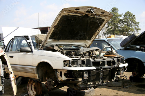Junker American auto in salvage yard with hood up.