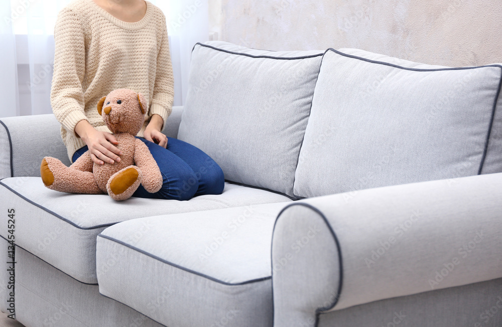 Young girl sitting with fluffy teddy bear on sofa in room Young girl sitting with fluffy teddy bear on sofa in room