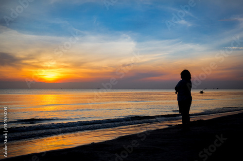 Woman stands at sunrise at the beach. © apichon_tee