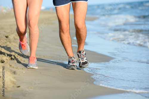 close up legs of young couple man and woman running in the sand on the shore of beach by the sea during sunny summer holiday vacation