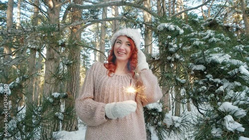 beautiful girl in the winter in the woods, winter nature,girl holding a sparkler, winter fairy tale, beautiful young woman standing near a big pine tree in a park, on a background of lot of snow photo