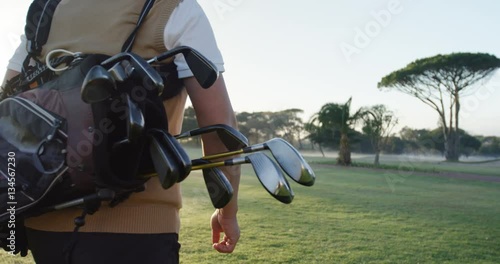 Golfer carrying his golf bag and walking on the golf course 