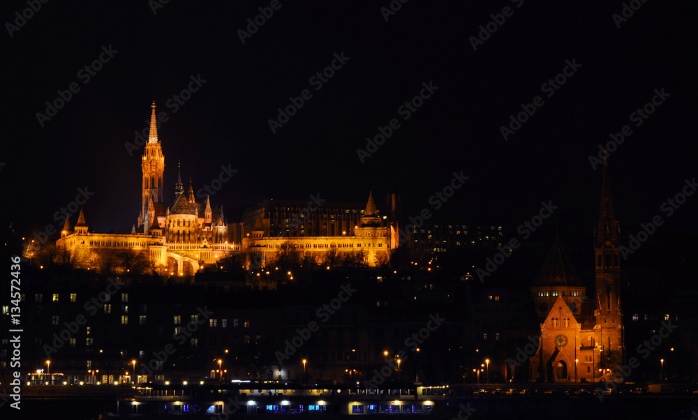 View on the illuminated Fisherman's Bastion and Calvinist Church on a winter night, surrounded by many lightened windows. Budapest