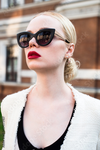 Happy Fashion blonde european elegant Woman with red lips and white skin Standing at the Old Red Brick building on green grass.  Beautiful Female in formal black and white dress. 