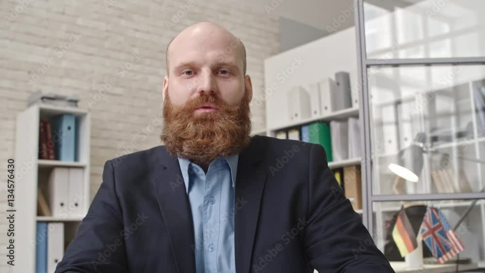 Bearded entrepreneur in formal suit sitting in the office and telling about something at the camera Bearded entrepreneur in formal suit sitting in the office and telling about something at the camera