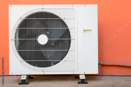 Condensing unit of air conditioner at a red-orange painted wall