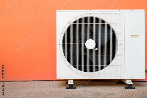 Foto Condensing unit of air conditioner at a red-orange painted wall