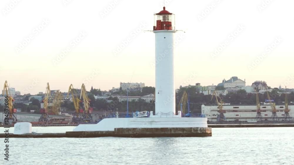 View on white lighthouse and port from sea with city on background in slowmotion View on white lighthouse and port from sea with city on background in slowmotion