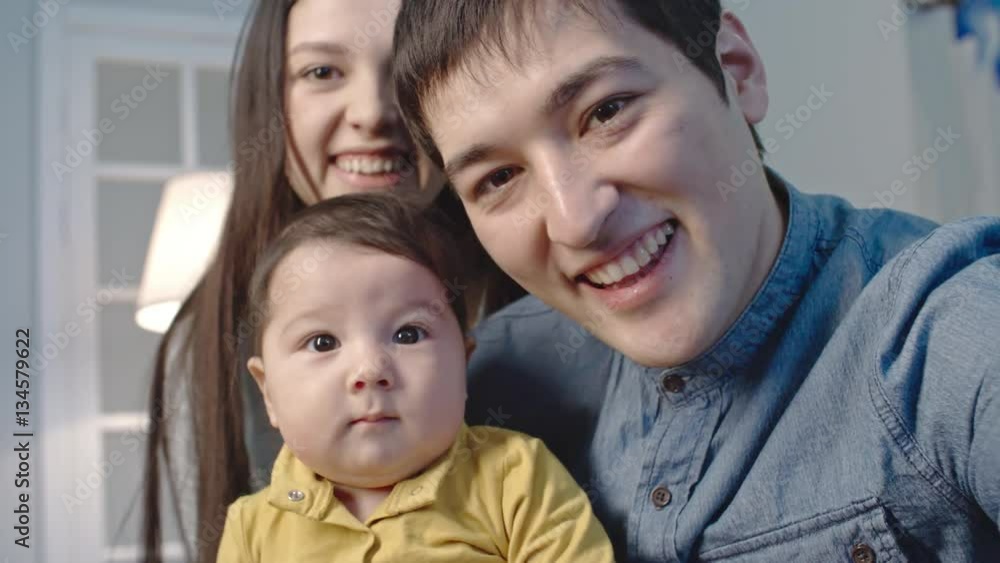 Loving dad and mom with little baby boy talking and waving at web camera while video calling somebody