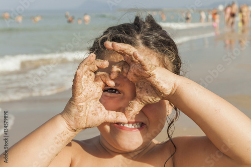 Girl looking through a heart draw with her hands. Beach. Summer