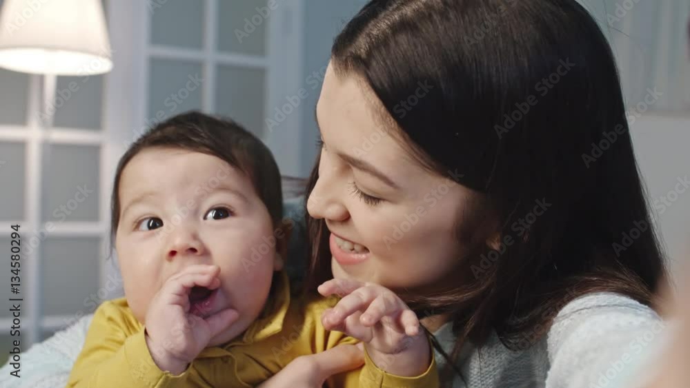Joyous young mother sitting with her baby son and telling something at camera with smile Joyous young mother sitting with her baby son and telling something at camera with smile