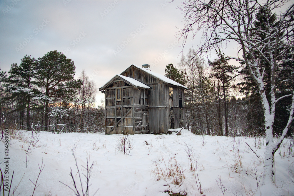 verfallenes Holzhaus mit verwitterter Fassade auf verschneiter Lichtung