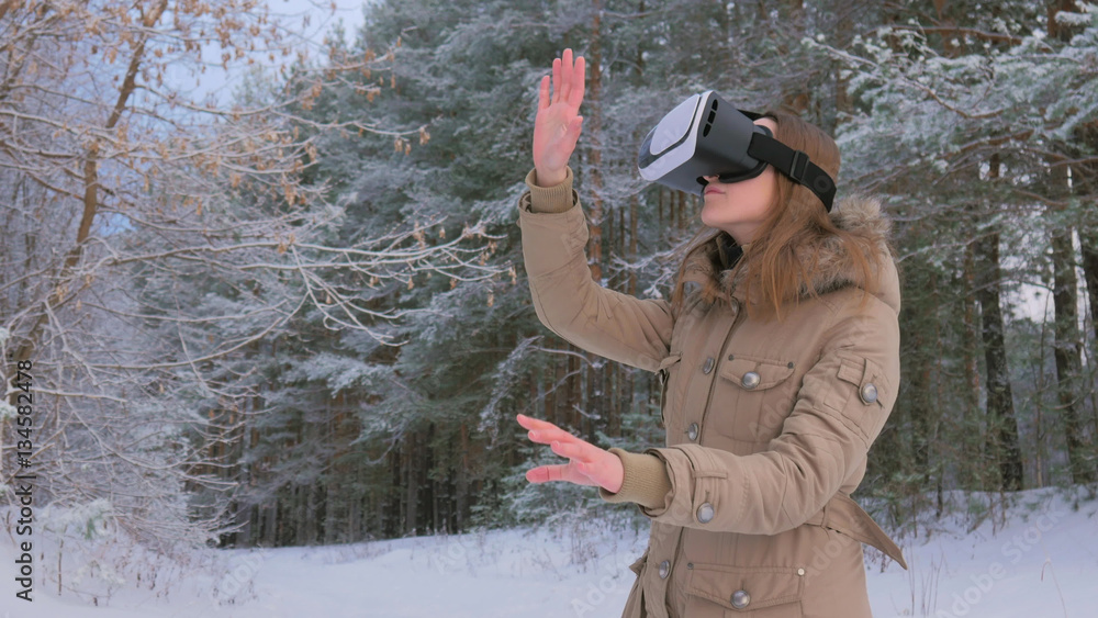 Woman putting on and using virtual reality glasses in winter forest. Virtual reality mask. VR. Future, nature, winter and technology concept