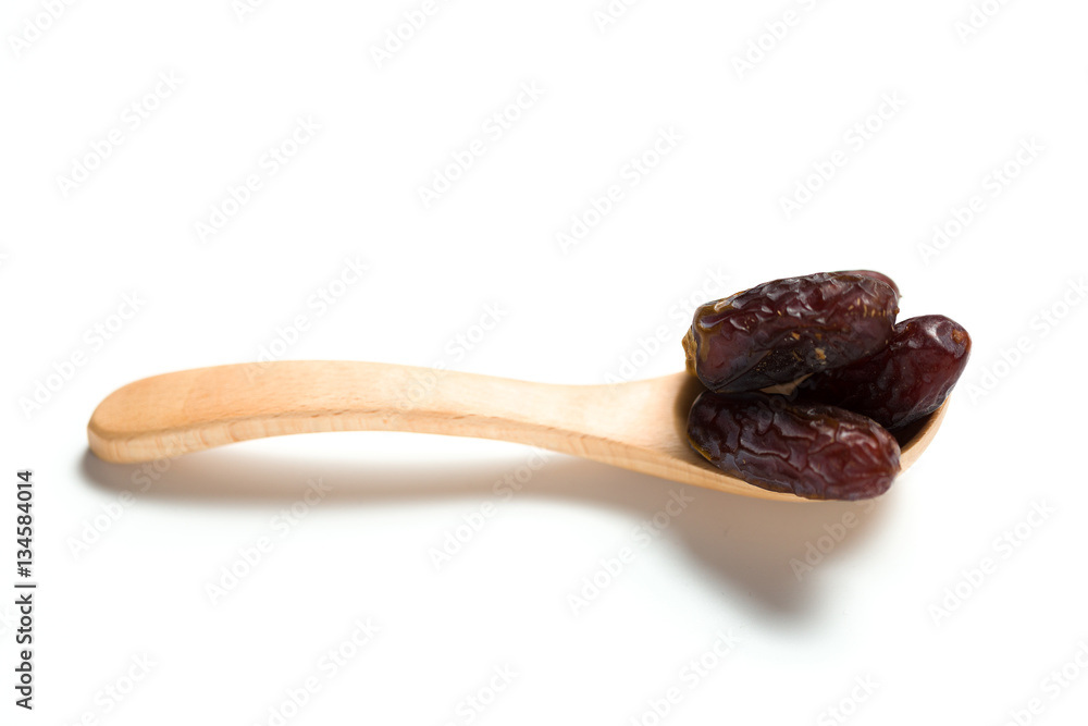 A dried dates in a wooden spoon isolated over white background A dried dates in a wooden spoon isolated over white background
