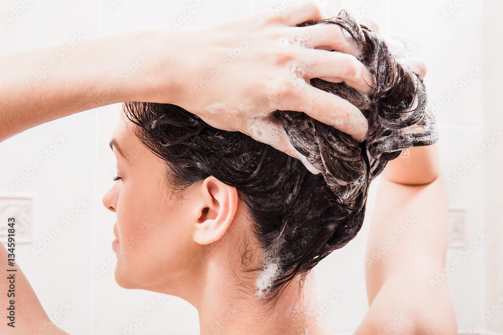 Fototapeta premium Young woman washing hair with shampoo in the shower
