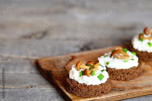 Fotografie Vegetarian canape with soft cheese and mushrooms on a board on a wooden table