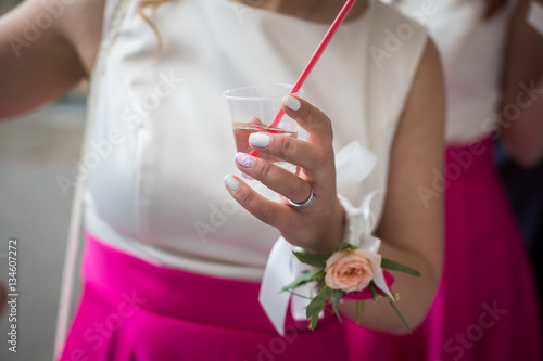 Bridesmaid in pink skirt holds plastic glass with a drink