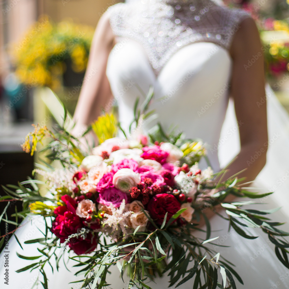 Bride in luxury wedding dress holds rich bouquet made of greener