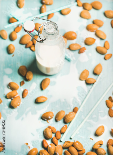 Dairy alternative milk. Almond milk in bottle and fresh nuts over blue background, selective focus, copy space. Clean eting, dairy-free, vegan, allergy-friendly, vegetarian, raw, healthy food concept photo