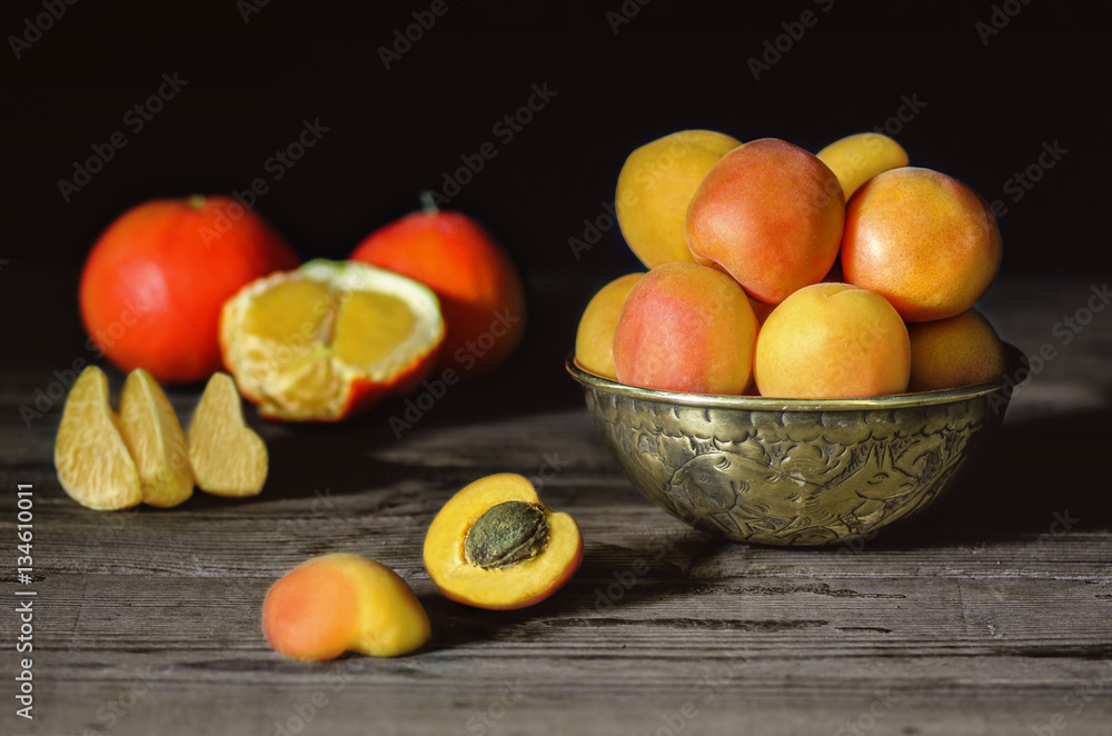Delicious fresh apricots placed in copper bowl with fresh tangerine on rustic wooden background.Close up