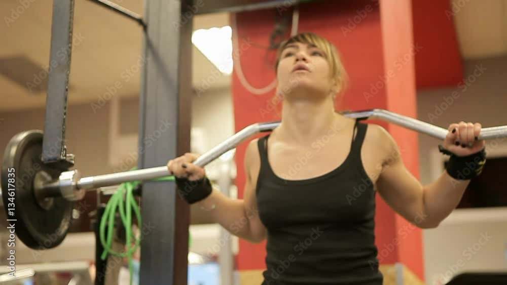 Squats in the gym. Paurlifting. Lifting. Squats with a weight. The woman trains in the gym. A training with a heavy weight. The woman squats. Lifestyle. Heavy weight