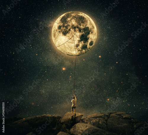 Imaginary view as a young man, holding a rope, try to catch and pull the full moon from the night sky. Achievement and hard determination concept. photo