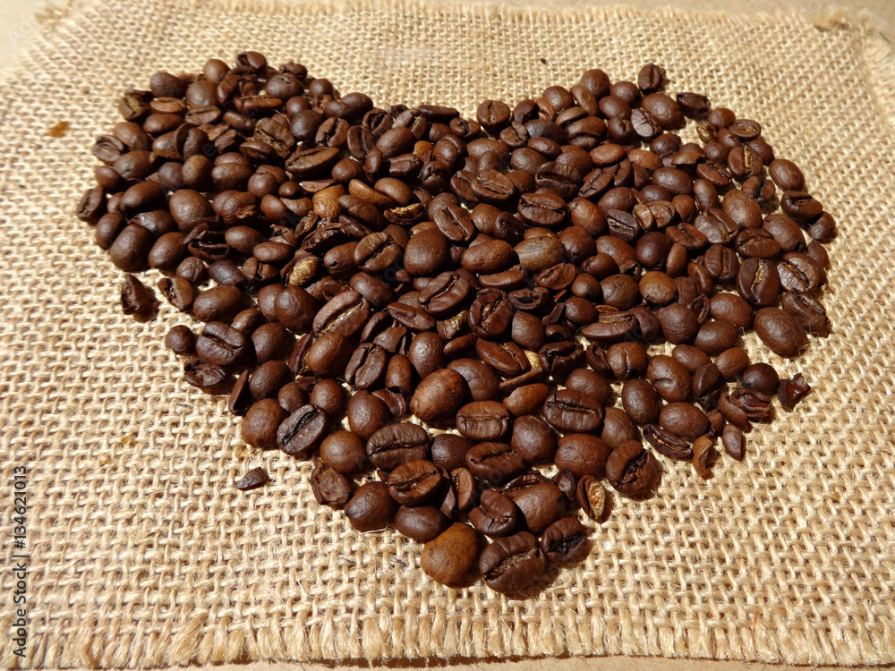 Fototapeta premium Кофейные зерна в форме сердца на фоне мешковины