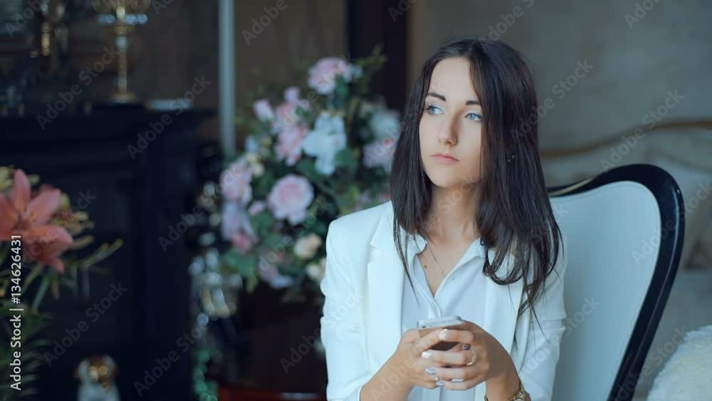 Woman texting with a smart phone sitting on a chair in the living room in a house interior Woman texting with a smart phone sitting on a chair in the living room in a house interior