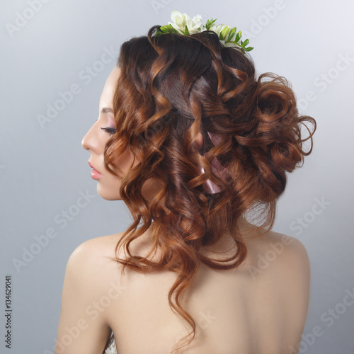 Beauty fashion portrait of a beautiful girl with a natural make-up and hairstyle with curls back isolated on a gray background.