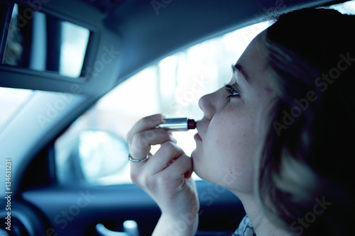 Girl paints her lips in a car behind the wheel